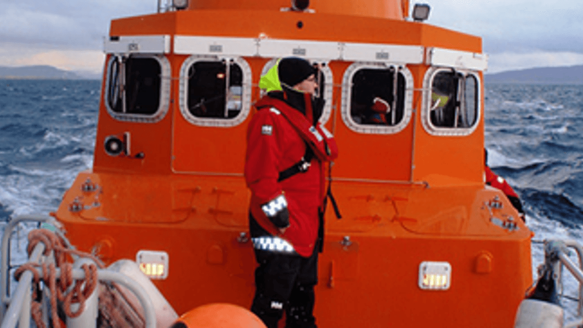 An orange life saving boat is out at sea with a crew member on deck