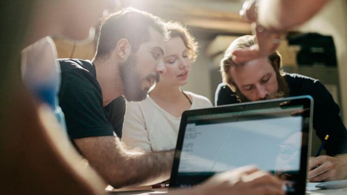 Three adults work on a laptop sharing ideas and making notes