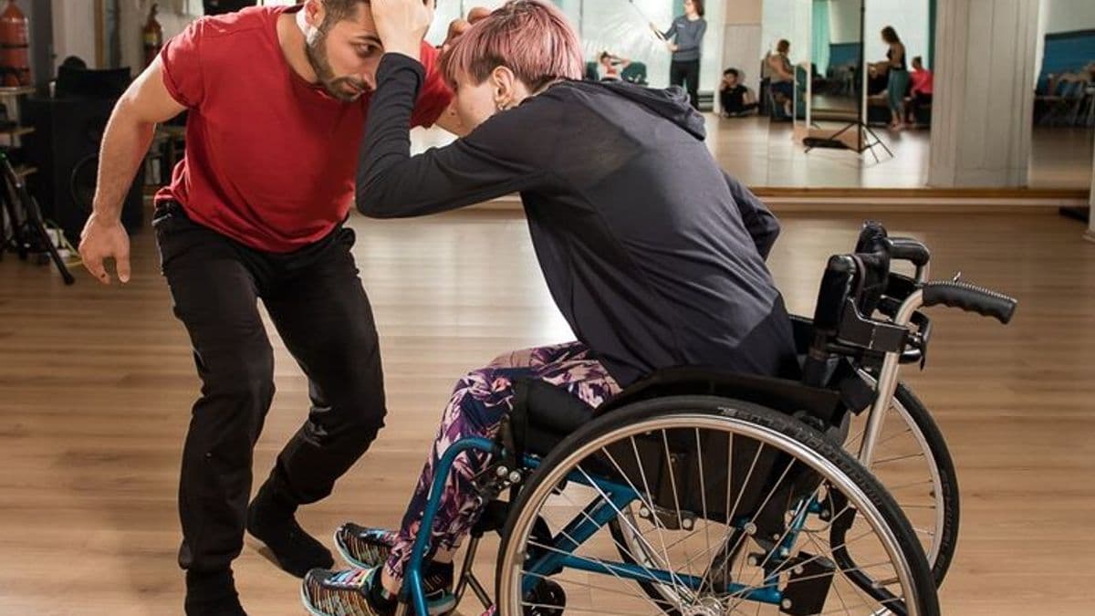 Within a gym setting, two young men fight as a sport; one is in a wheelchair, the other is on his feet