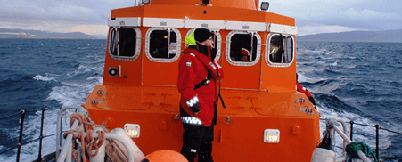An orange life saving boat is out at sea with a crew member on deck