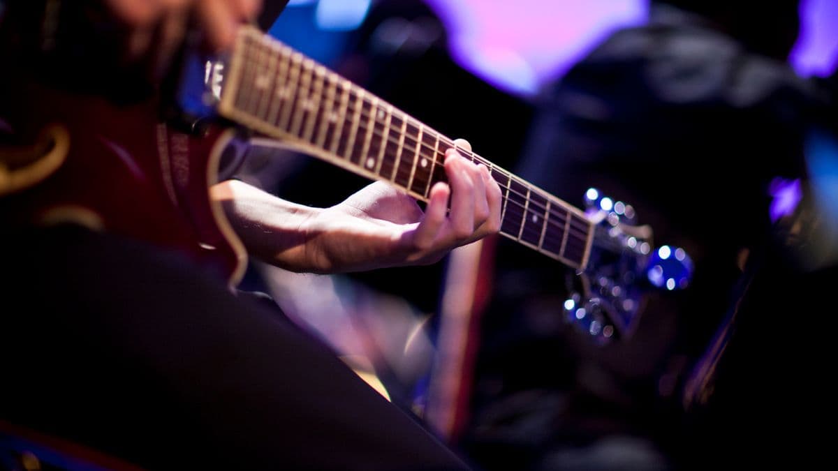 Llun agos o law cerddor yn chwarae gitar.