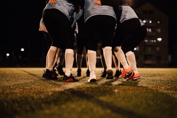 Low section of female soccer team huddling together on field at night