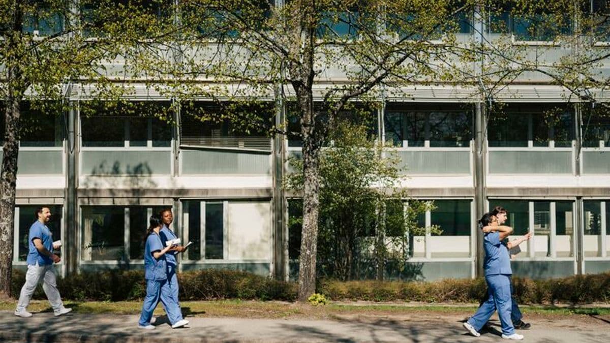 Full length of medical team talking with each other while walking on lawn in front of hospital building at sunny day