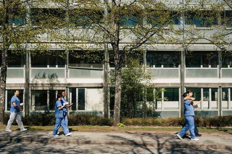 Full length of medical team talking with each other while walking on lawn in front of hospital building at sunny day