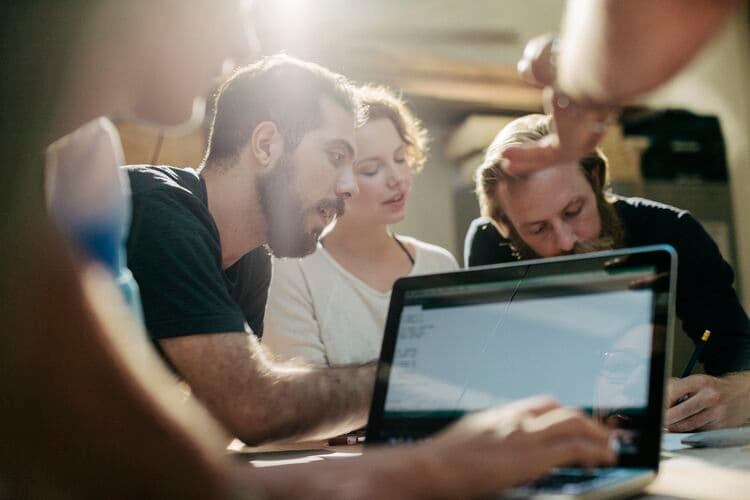 Three adults work on a laptop sharing ideas and making notes