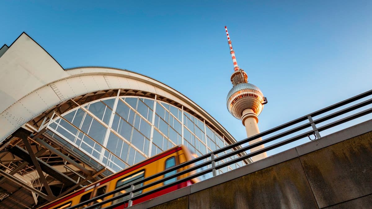 Tren yn gadael gorsaf Aleksanderplatz yn Berlin gyda'r twr teledu yn y cefndir.