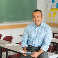 Teacher sitting on desk holding a school book smiling